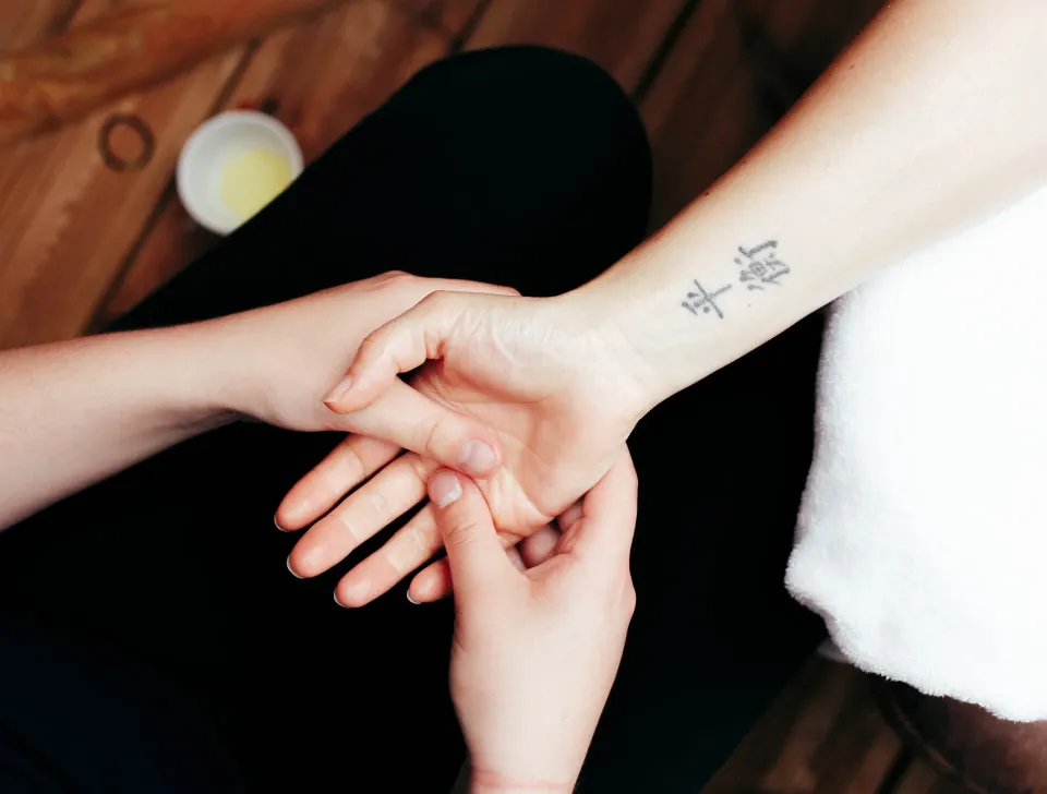 Zwei Hände halten ein Handgelenk mit einem Tattoo auf einem Holztisch mit einer Schüssel Sahne