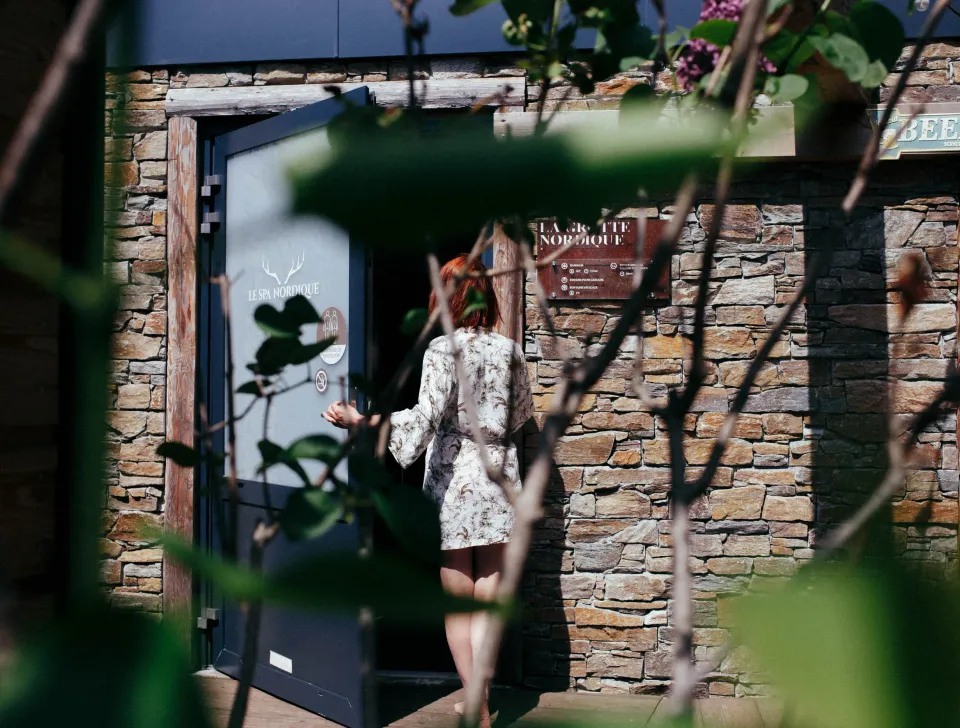 Eine Frau in einem weißen und roten Kleid betritt ein Steingebäude mit einer Glas Tür, auf der "Le Chalet Nordique" steht.