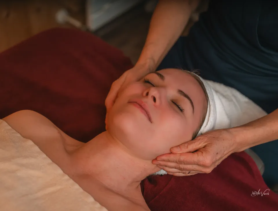Eine Person, die auf dem Rücken liegt, erhält von einer anderen Person eine Gesichtsmassage.